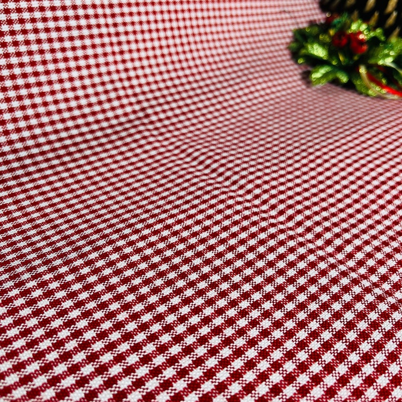 May include: A close-up of a red and white checkered fabric. The pattern is a classic gingham design, with small squares of red and white. The fabric is slightly wrinkled, suggesting it is a tablecloth or similar textile.