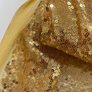 May include: Gold sequin fabric with a sheer mesh backing. The sequins are small and densely packed, creating a shimmering effect.
