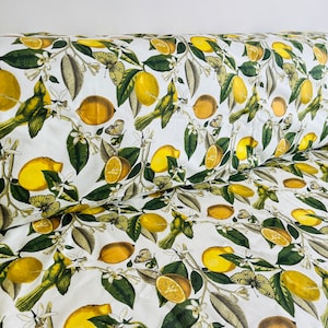 May include: White fabric with a repeating pattern of yellow lemons, green leaves, and butterflies. The fabric has a subtle texture.