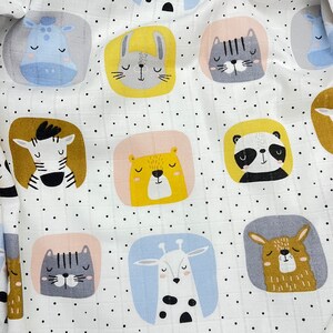 May include: White fabric with a repeating pattern of cartoon animal faces, including a zebra, panda, and cat, each within a colored square. The background has small black polka dots. The fabric is likely for baby items.