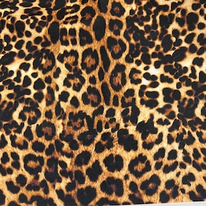 May include: A close-up of a brown and black leopard print fabric. The fabric has a textured surface and a repeating pattern of black spots on a brown background.