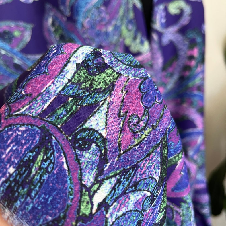 May include: Close-up of a purple fabric with a paisley pattern in shades of pink, blue, and green.