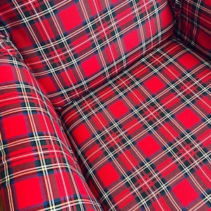 May include: An armchair upholstered in a vibrant red fabric featuring a classic tartan plaid pattern. The textile design consists of intersecting horizontal and vertical lines in shades of dark green, navy blue, white, and yellow against a bright red base.