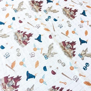A white fabric with a repeating pattern of themed illustrations. The illustrations include a castle, an owl, a key, a potion bottle, a lightning bolt, a pair of glasses, a hat, and a wand. The fabric is a light cream color with a subtle grid pattern.