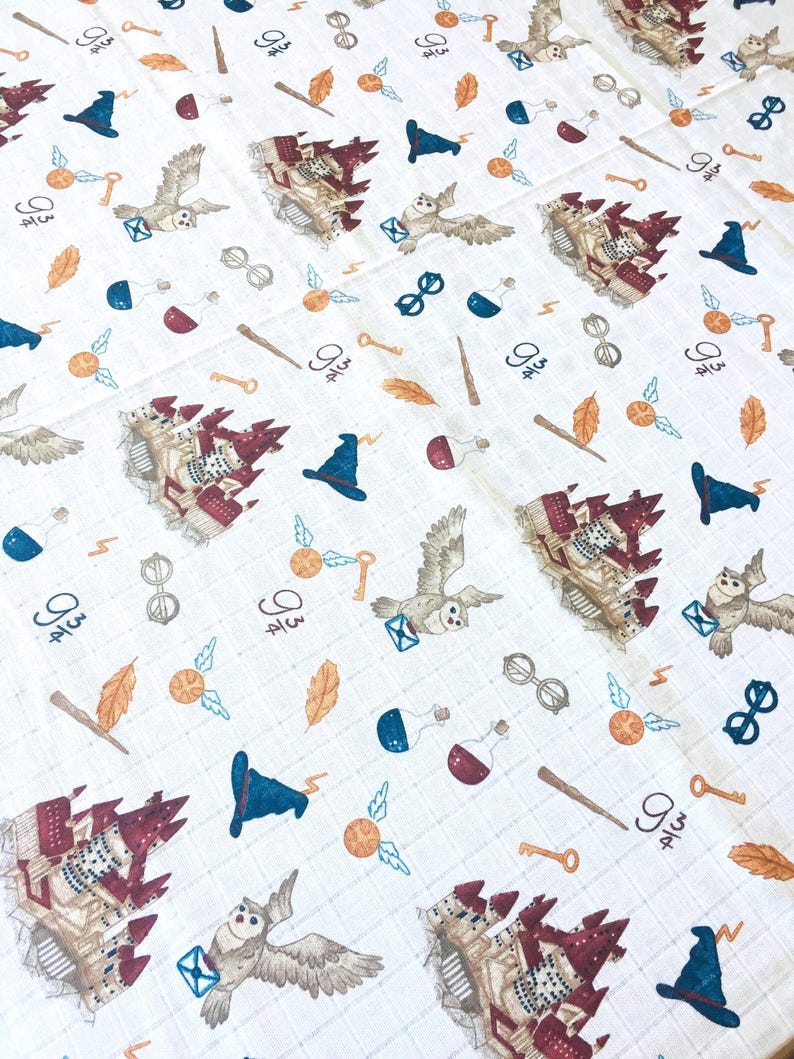A white fabric with a repeating pattern of themed illustrations. The illustrations include a castle, an owl, a key, a potion bottle, a lightning bolt, a pair of glasses, a hat, and a wand. The fabric is a light cream color with a subtle grid pattern.