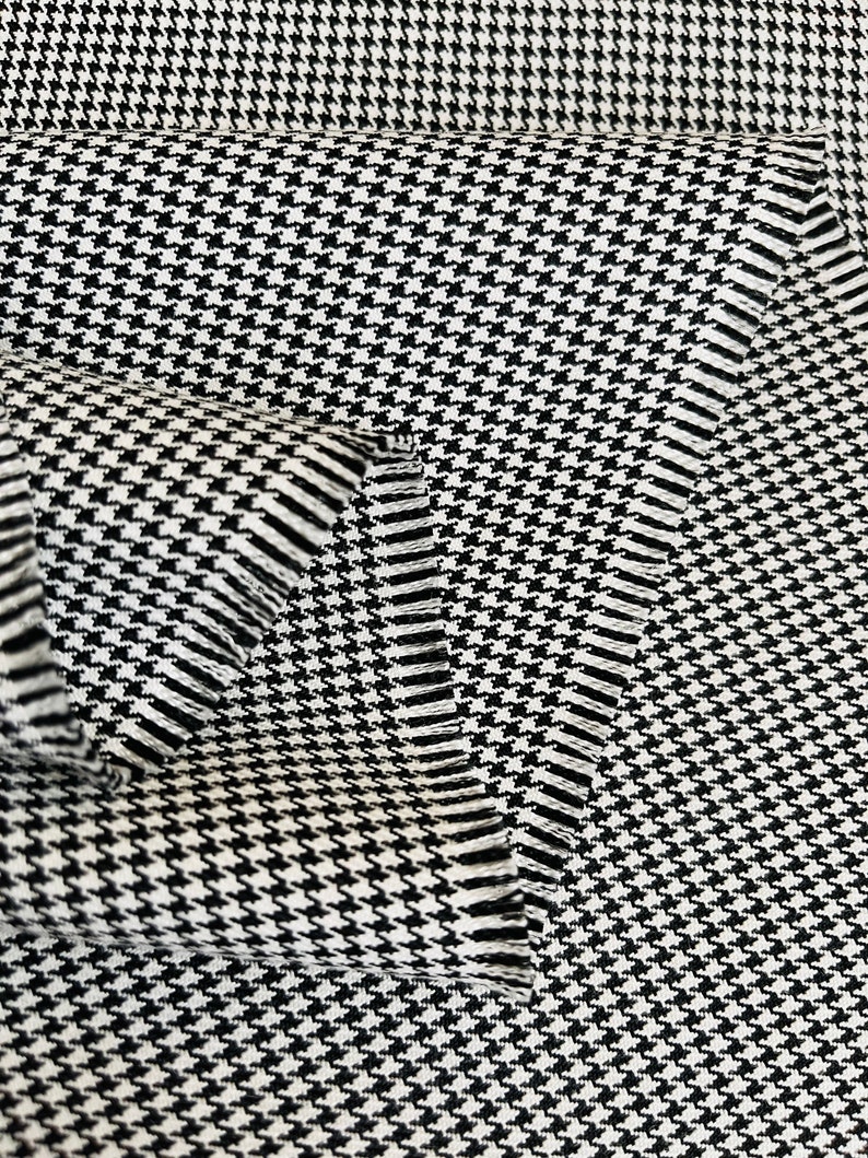 May include: Black and white houndstooth fabric with a textured weave. The fabric is folded over itself, showing the edges.