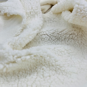 May include: Close-up of a white faux fur fabric with a soft, fluffy texture.