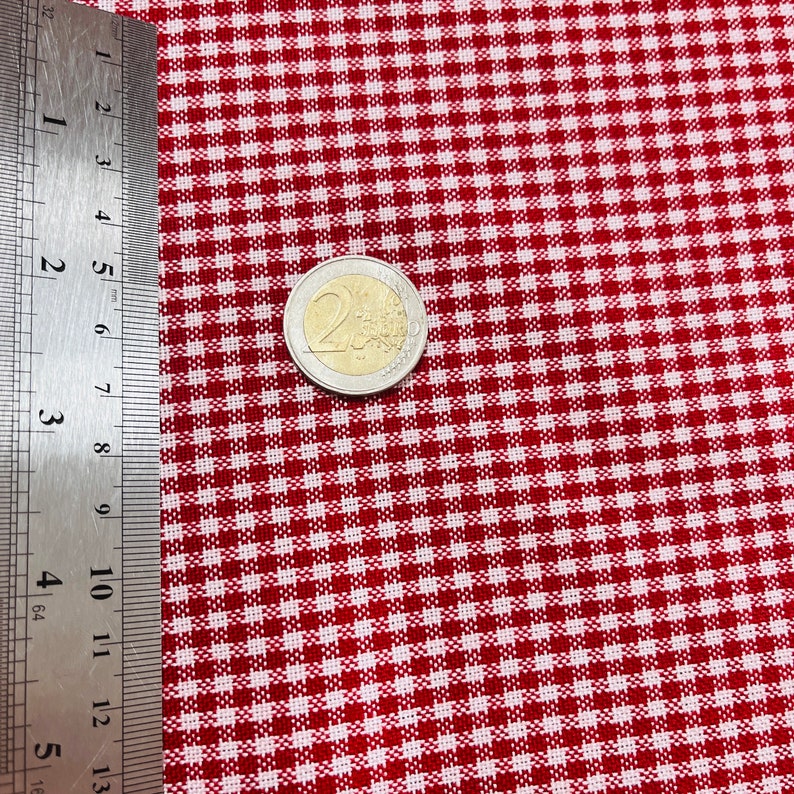 May include: Close-up of red and white checkered fabric. A silver and gold two-euro coin is on the fabric. A metal ruler is on the left side of the fabric, showing measurements in inches.