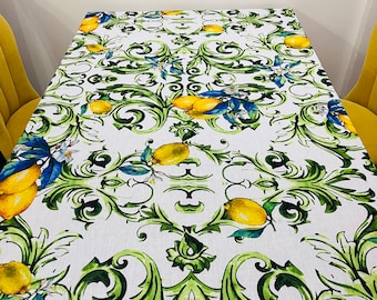 May include: White tablecloth with a vibrant lemon and foliage pattern. The design features yellow lemons, blue leaves, and green vines. The tablecloth is spread across a table, creating a fresh and inviting look.