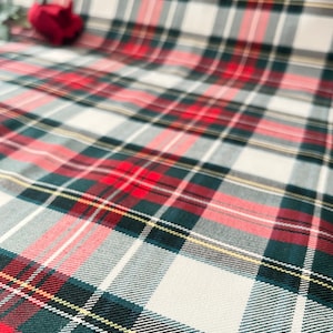 May include: A red, white, and green plaid fabric with a subtle yellow stripe. The fabric has a woven texture.