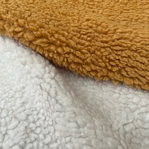 May include: Two pieces of fabric with a fuzzy texture. One piece is a light brown color and the other is white.