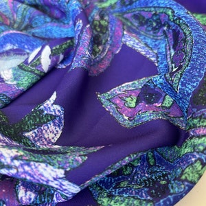 May include: Purple fabric with a colorful floral pattern. The flowers are stylized and have a pixelated appearance. The fabric is soft and has a silky texture.