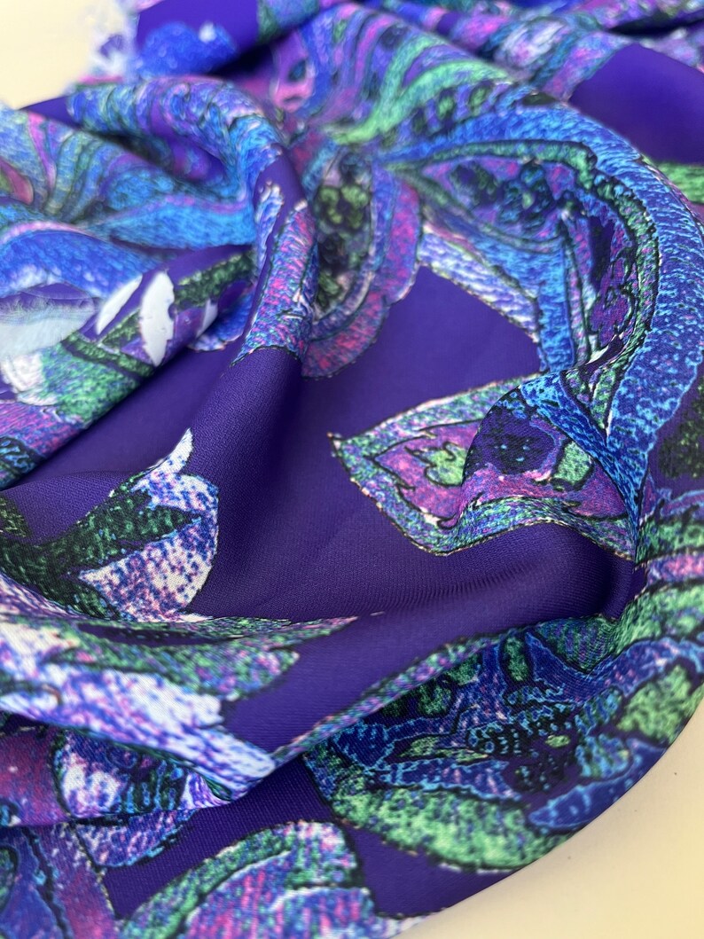 May include: Purple fabric with a colorful floral pattern. The flowers are stylized and have a pixelated appearance. The fabric is soft and has a silky texture.