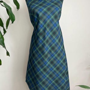 May include: A length of fabric draped over a mannequin, featuring a diagonal plaid pattern in shades of dark blue, forest green, and black, accented with thin, intersecting lines of bright yellow and red throughout the textile design.