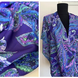 May include: Purple fabric with a paisley pattern in shades of blue, green, and pink. The fabric is shown draped over a mannequin.