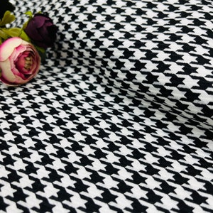 May include: Black and white houndstooth fabric with a subtle texture. The fabric is folded and draped, showing the pattern.