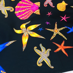 May include: A black fabric with a repeating pattern of colourful starfish and seashells. The starfish are decorated with rhinestones and the seashells are decorated with gold accents.