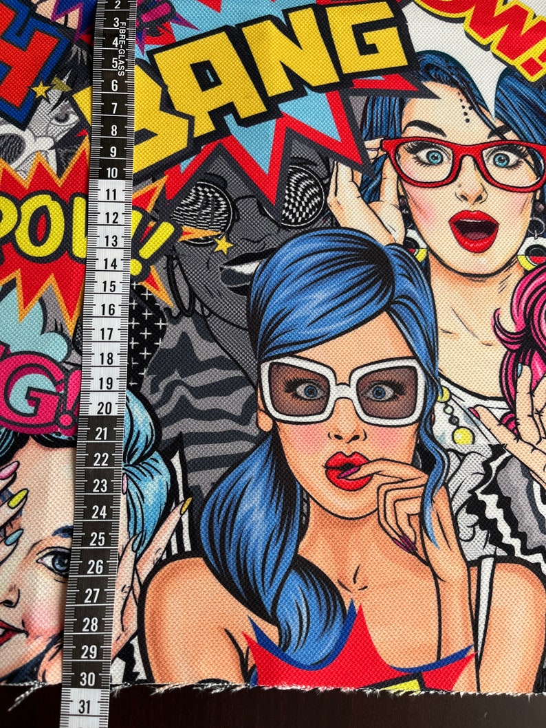 May include: A colorful fabric with a pop art design featuring women with bold makeup and sunglasses. The fabric has a textured surface and includes the words "BANG" and "POW!" in large, bold letters.