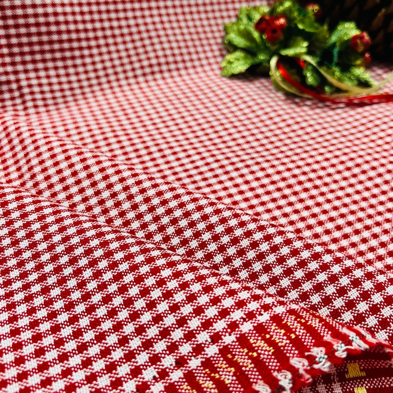 May include: Close-up of red and white checkered fabric. The fabric is folded, showing the texture and pattern. The pattern is a classic gingham design, with small squares of red and white. The fabric is likely cotton or a similar material.