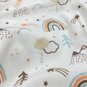 May include: White fabric with a repeating pattern of brown, blue, and peach rainbows, stars, mountains, clouds, and trees.