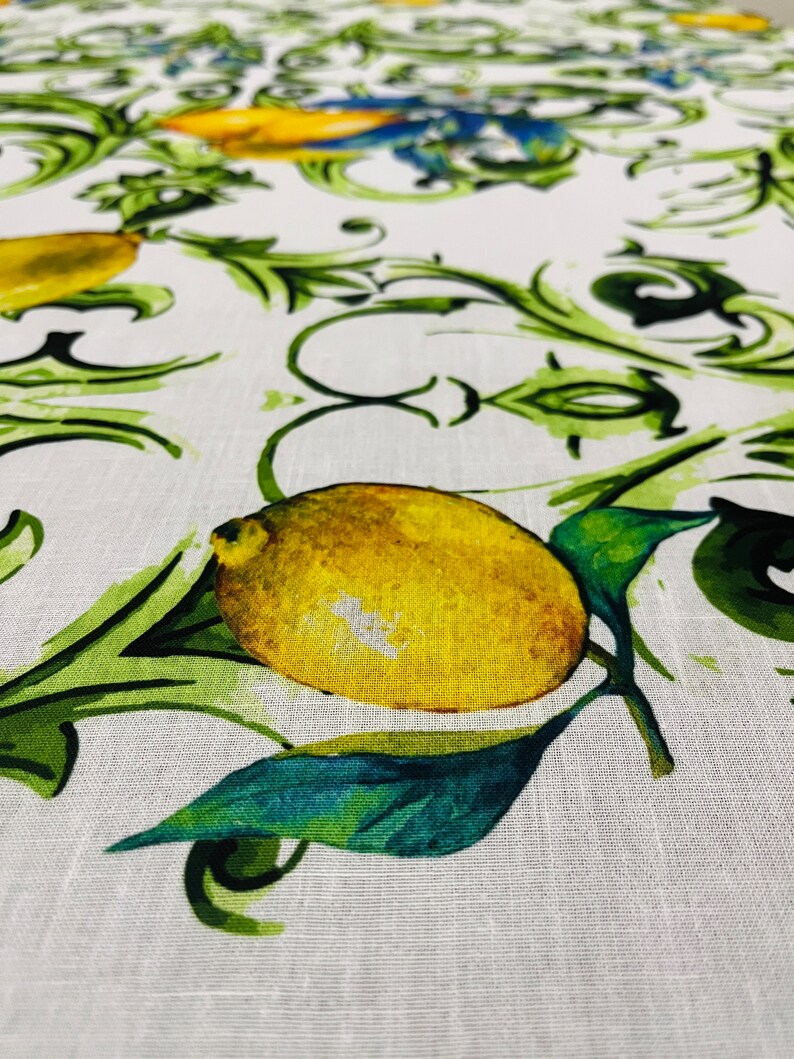 Puede incluir: Primer plano de un mantel blanco con un patr&oacute;n repetido de limones amarillos, hojas verdes y vides verdes onduladas. Los limones est&aacute;n detallados con sombreado, y las hojas tienen un efecto de acuarela. La tela tiene una textura de lino.