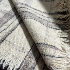 May include: A folded, off-white blanket with a plaid pattern in shades of gray and black. The blanket has a fringed edge. The fabric appears to be a soft, woven material.