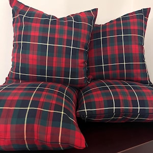 May include: Four square throw pillows featuring a classic tartan plaid pattern in shades of deep red, dark navy blue, and forest green, accented with thin yellow lines. Each pillow has a visible side zipper closure along the bottom edge.