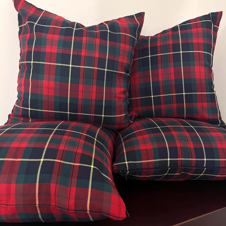 May include: Four square throw pillows featuring a classic tartan plaid pattern in shades of deep red, dark navy blue, and forest green, accented with thin yellow lines. Each pillow has a visible side zipper closure along the bottom edge.