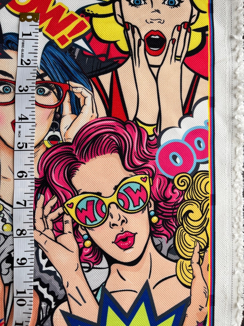 May include: Colorful fabric with a pop art design featuring three women with exaggerated features. The women are wearing sunglasses, red lipstick, and have pink, blonde, and blue hair. The fabric has a white background with black outlines and the word "WOW" in yellow letters.