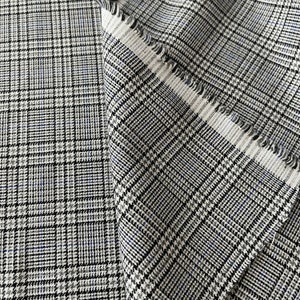 May include: Close-up of a white fabric with a black and blue plaid pattern. The fabric is folded over itself, showing the texture of the weave.