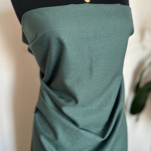 May include: A dark teal fabric draped over a black mannequin. A gold-toned necklace with a floral design and a teardrop pendant is displayed on the mannequin. The fabric has a subtle texture.