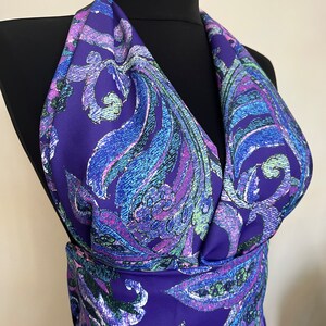 May include: Purple fabric with a paisley pattern in shades of blue, green, and pink. The fabric is draped over a black mannequin.