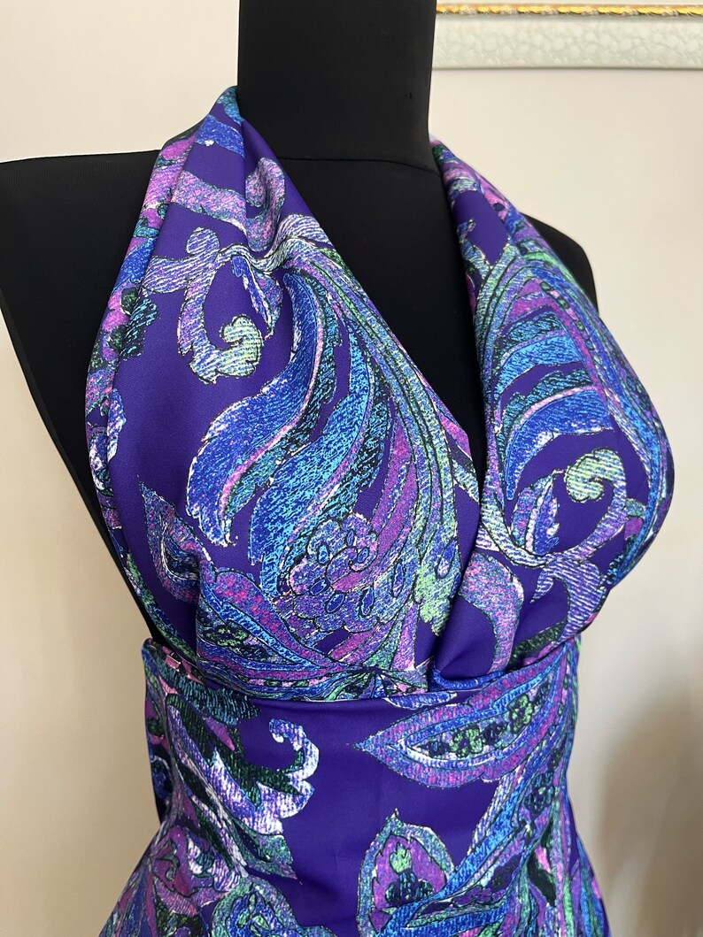 May include: Purple fabric with a paisley pattern in shades of blue, green, and pink. The fabric is draped over a black mannequin.