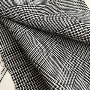 May include: Black and white houndstooth fabric with a woven pattern. The fabric is folded and shows the texture of the material.