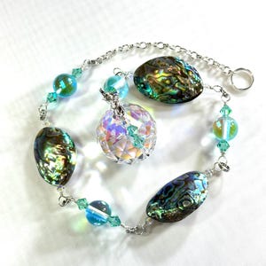 Può includere: Un acchiappasole di cristallo con accenti di conchiglia di abalone iridescente e perline di vetro turchese appese a una catena d'argento.