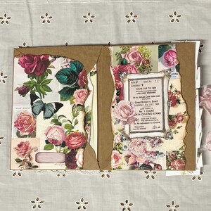 Pu&ograve; includere: Un album con copertina marrone e pagine decorate con motivi floreali, tra cui rose, farfalle e un biglietto vintage per la Coppa Davis.