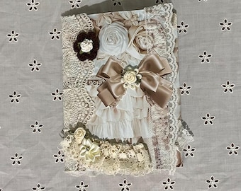 Può includere: Una copertina per album di ritagli decorativi con un design floreale con rose bianche, bordatura in pizzo marrone e un fiocco di raso marrone con un accento di fiore bianco.
