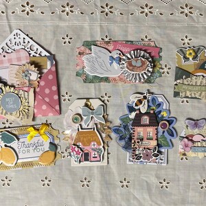Peut inclure: Une collection d'embellissements artisanaux en papier colorés avec divers thèmes, notamment une maison, un oiseau, un citron et un cœur. Les embellissements sont décorés de fleurs, de feuilles et d'autres détails. Le texte "Best of Times", "Thankful for You", "My heart is happy", "Calm Blue Skies", et "Happy" est visible sur les embellissements.