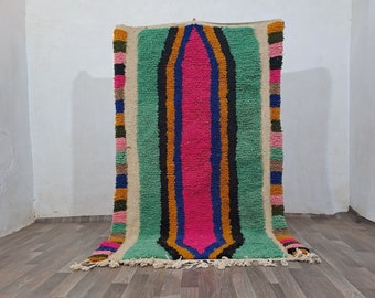 May include: A colorful Moroccan rug with a green, pink, orange, and blue striped pattern. The rug is made of wool and has a fringe on the ends.