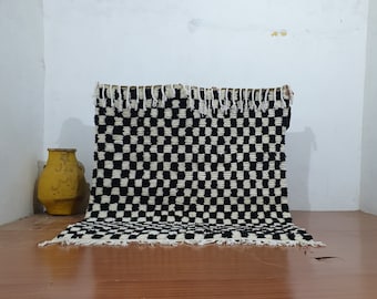 May include: Black and white checkered rug with fringe on the edges. The rug is laying on a wooden floor.