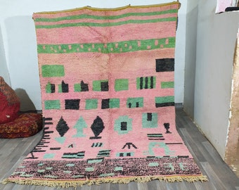 May include: A pink and green Moroccan rug with a geometric pattern. The rug has a fringe border and is made of wool.