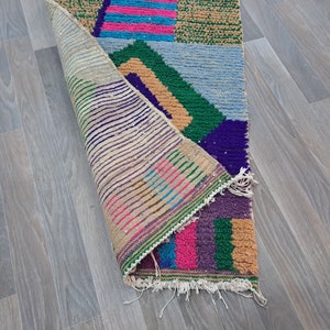 May include: A colorful, geometric patterned rug with a fringed edge. The rug is folded in half, revealing the back side, which is a beige color with a striped pattern.