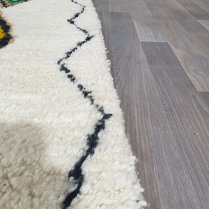 May include: A close-up of a white, textured rug with a black zigzag pattern and colorful geometric shapes. The rug has a thick pile and a soft appearance, suitable for home decor.