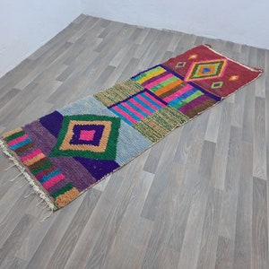 May include: A colorful Moroccan rug with geometric patterns in shades of pink, green, blue, and yellow. The rug has a fringed edge and is made of wool.