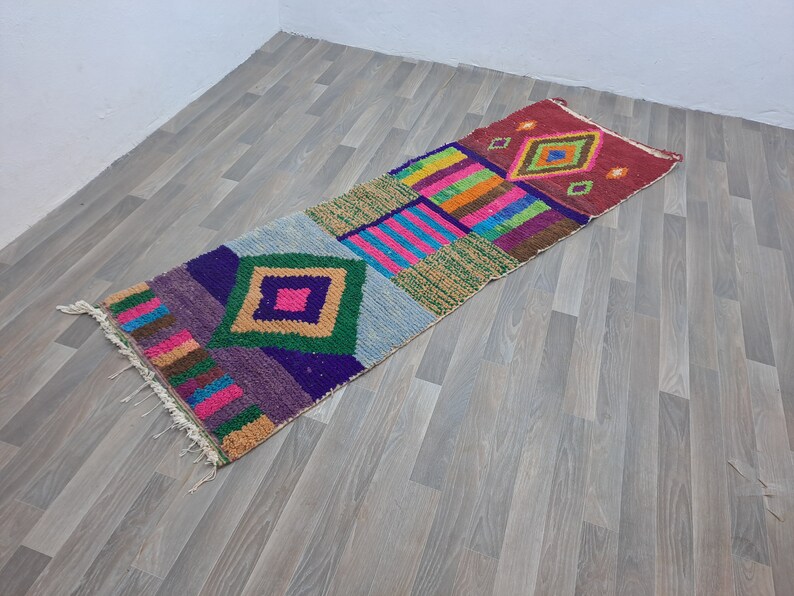 May include: A colorful Moroccan rug with geometric patterns in shades of pink, green, blue, and yellow. The rug has a fringed edge and is made of wool.