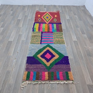 May include: A colorful, geometric patterned rug with a diamond shape in the center. The rug is made of woven wool and has a fringe on the ends.