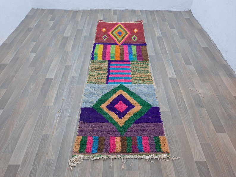 May include: A colorful, geometric patterned rug with a diamond shape in the center. The rug is made of woven wool and has a fringe on the ends.