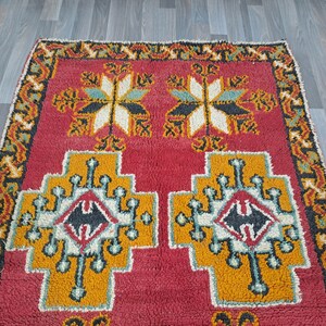 K&ouml;nnte beinhalten: Ein roter, orangefarbener, schwarzer und wei&szlig;er marokkanischer Teppich mit geometrischem Muster. Der Teppich hat einen Fransenrand.