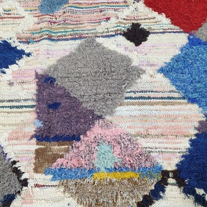 May include: A colorful, hand-woven rug with a patchwork design. The rug features various colors, including blue, red, pink, and gray, and is made with a variety of textures. The rug is perfect for adding a touch of bohemian style to any room.