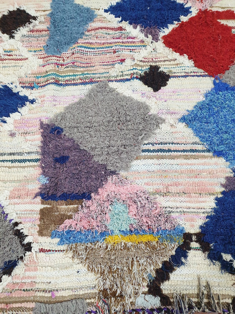 May include: A colorful, hand-woven rug with a patchwork design. The rug features various colors, including blue, red, pink, and gray, and is made with a variety of textures. The rug is perfect for adding a touch of bohemian style to any room.